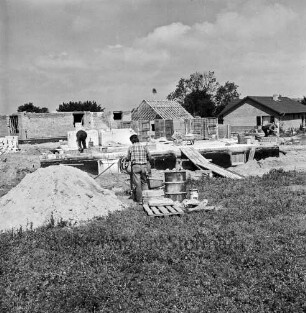 Dienstleistungszentrum: Oetjendorfer Kirchenweg / Am Schwarzen Berg: Bau: vorn links Sandhaufen: daneben Arbeiter an der Mischmaschine: hinten weitere Arbeiter auf Fundament: hinten Grundmauern: dazwischen Baumaterial: hinten Einfamilienhäuser nach Fertigstellung und im Rohbau