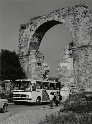 Ein moderner Bus fährt durch das alte Stadttor neben dem Theater, Side