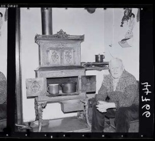 Alter Mann in seiner Wohnküche vor einem Ofen aus Gußeisen