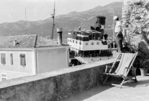 Dampfschiff : Blick von einer Terrasse auf ein an der Stadt vorbei fahrendes Schiff.