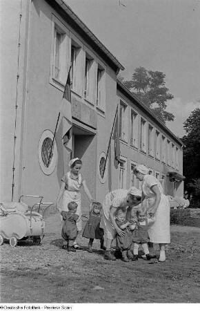 Pflegerinnen mit Kindern vor dem Heimgebäude