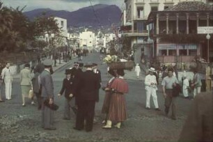 Denkmal für João Gonçalves Zarco : Reisefotos Madeira. Funchal. Avenida Zarco mit Café Kit Kat. Straßenbild mit Passanten gegen das Denkmal für João Gonçalves Zarco. Bronze (1934; F. Franco)
