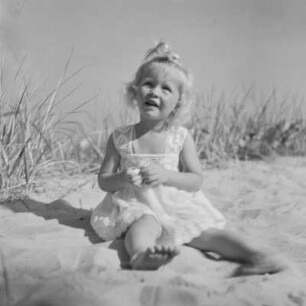Kleines Mädchen mit Kleid sitzt und spielt am Strand