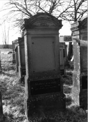 Grabstein 94 (Index: 100116254) Material: Sandstein, Granitplatte Zustand: Schriftplatte an der Stele fehlt Maße HxBxT: 266x64x27 cm Beschreibung: doppelt aufgesockelte Stele mit doppeltem, eingezogenem Segmentbogenabschluß, Schriftplatte aus Stele und oberem Sockel, Schriftfeld auf der Rückseite: Grabstein 94