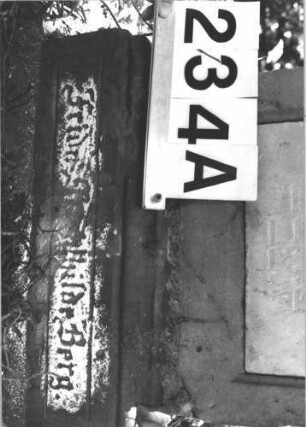 Grabstein 234 (Index: 100082185) Material: Sandstein, weiße Marmorplatte Zustand: beschädigt, verwittert mit Textverlust Maße HxBxT: 101x60x30 cm Beschreibung: Stele, profiliert. Sockel, Volutenaufsatz m. Mittelakroter, rechteck. Schriftplatte Symbolik: Voluten, Blüten, Ranken: Grabstein 234A