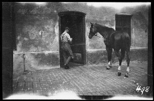 Nicht identifizierbare Ortschaft (Dep. Somme (?), Frankreich): schwarzes Pferd mit weißen Fesseln und ein Pferdebursche vor einem Hauseingang