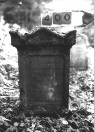 Grabstein 400 (Index: 99799630) Material: Sandstein Zustand: verwittert Maße HxBxT: 96x57x18 cm Beschreibung: Stele, Abdeckplatte mit Giebelaufsatz u. Seitenakroteren, Schriftfeld eingetieft, Sockel: Grabstein 400