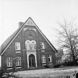 Bauernhaus: Blick auf Giebelfront mit Eingang und Verzierungen: rechts Baum: davor Rasenfläche: hinten rechts Gebäude
