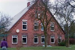 Hörn 23: Hofanlage: traufständiges Bauernhaus aus Backstein von 1874: Giebelseite Wohntrakt: Fenster, unter Ortgang Treppenfries: davor zwei Bäume: vorne links Mann [Rückenansicht]