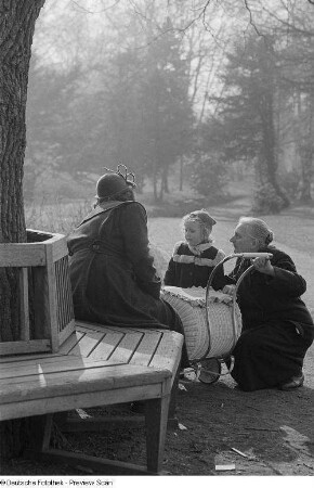Eine Frau und ein Mädchen sowie eine Frau auf einer Parkbank mit Kinderwagen