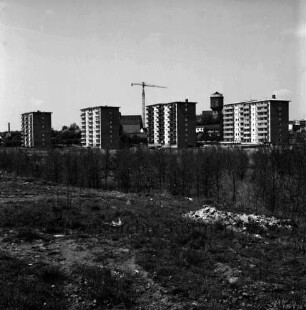 Stoltenrieden: Blick von Industriestraße Richtung Bahnhof: vorn unbefestigtes Gelände mit Bauschutt: dahinter Baumreihe und vier Wohnblocks: im Hintergrund Mitte Baukran und Silo der Johannes Ströh Mühlenwerke, rechts Wasserturm