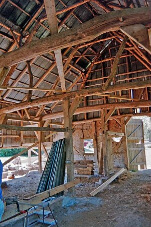 Dorfplatz (2): Fachwerkscheune: Sanierung: Innenansicht: nach Entkernung: Ständergerüst, Dachstuhl: hinten Scheunentor, Außenwand teilweise von Entfernung der Ausmauerung: oben Blechverkleidung: Baumaterialien: Juli 1994