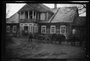 Rasziuny (?) (=Rašèiūnai, Litauen): stattliches Holzhaus (Quartier?) mit umbauter Mittelveranda und Balkon darüber und Vierspänner mit Personenwagen davor