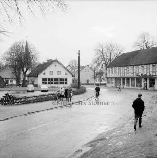 Kirchenstraße: links Volksschule mit Schulhof und Parkplatz: dahinter Martin-Luther-Kirche und Bäume: hinten rechts Gasthof und Hotel "Holländer": vorn rechts und Mitte Fußgänger und Fahrradfahrer: im Hintergrund Wohn- und Geschäftshäuser