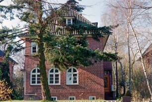 Struhbarg 12: giebelständiges Wohnhaus aus Backstein mit umlaufendem Gesims: Straßenfront mit Rundbogen-Sprossenfenstern: rechts an Traufseite Eingangsvorbau, Treppe: Vorgarten, Baum