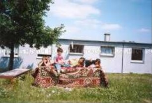 Vier Kinder auf einem mit einem Teppich bedeckten Tisch auf einer Wiese (Altersgruppe bis 14)