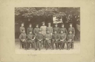 15 Offiziere je in Uniform mit Mütze, stehend oder sitzend in Garten