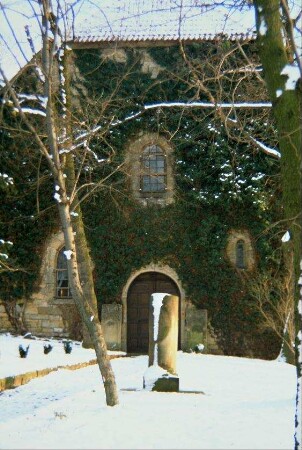 Westfassade der Gottesackerkirche, Efeu bewachsen; alte Grabsäule