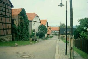Straße mit Reihe giebelständiger Häuser; Gartenzaun und Fußweg