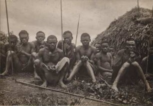Gruppenportrait : Gruppenportrait mit zehn Männern, die vor einer Hütte sitzen