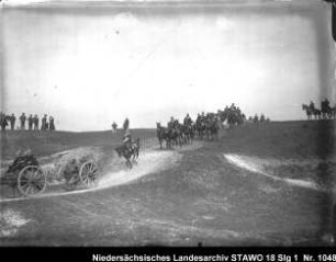 Besichtigung des Feld-Artillerie-Regiments Nr. 46 (?) Enthält: Soldaten auf mit Pferden bespannten Geschützlafetten und berittene Soldaten reiten eine Anhöhe hinunter, im Hintergrund: Zuschauer