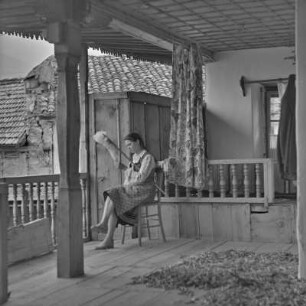 Veranda eines Wohnhauses in Bansko. Frau in bulgarischer Tracht übt das Handwerk des Spinnens aus