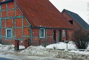 Hauptstraße (18): giebelständige Fachwerkkate: Traufseite mit zwei Türen: links Straßenfront Wirtschaftstrakt [angeschnitten]: davor Zaun, Gartenpforte: hinten rechts Neubau