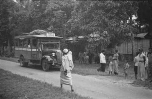Haltestelle der Autobuslinie von Medan nach Padang : Dorfstraße mit Personen, Hütten und Autobus