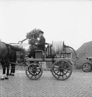 Freiwillige Feuerwehr Stubbendorf: Handdruckspritze von 1907 mit Pferdegespann: darauf zwei Feuerwehrmänner in Uniform: vorn Kopfsteinpflaster: hinten rechts Vorderrad eines Motorrades: hinten Häuser und Bäume