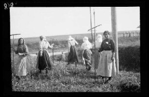 Bei Origny (?) (=Origny-Sainte-Benoite, Dep. Aisne, Frankreich): Frauen mit Holzrechen auf einem Feld (Distanzaufnahme) ("Frauen bei der Ernte")
