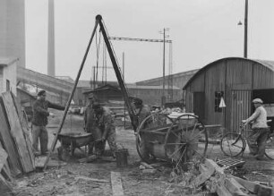 Industrie-Kraftwerk. Entschlammen der Kanalisation (?). Arbeiter mit Dreibock-Seilwinde an einem Kanalschacht : Lauta (Niederlausitz). Industrie-Kraftwerk. Entschlammen der Kanalisation (?). Arbeiter mit Dreibock-Seilwinde an einem Kanalschacht
