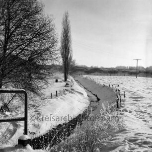 Norderbeste: Zäune auf Uferböschung: vorn links Geländer: daneben Gesträuch: dahinter Bäume: hinten links Häuser: Winter