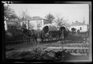 Odobești (=Rumänien): Zweispänner mit Planwagen auf einer unbefestigten Ortsstraße, im Vordergrund ein massiver Holzsteg, im Hintergrund repräsentative Gebäude