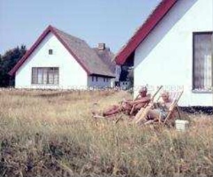 Urlauber entspannen vor reetgedecktem Haus auf der Ostseeinsel Hiddensee