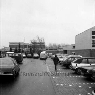 Grund- und Hauptschule Bargteheide-Land [früher Dörfergemeinschaftsschule, später Johannes-Gutenberg-Schule]: Alte Landstraße: vorne Parkplatz, parkende Autos, Person