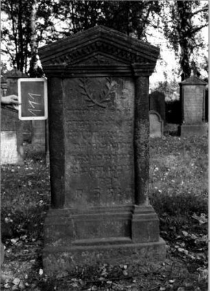 Grabstein 111 (Index: 100111230) Material: Sandstein Zustand: verwittert Maße HxBxT: 145x70x19 cm Beschreibung: ädikulaartige Stele mit Halbsäulen, getreppter Sockel, giebelartiger Abschluß mit Verdachung Symbolik: gekreuzte Zweige, Blüte, Zackenfries Besonderheit: Kindergrab: Grabstein 111