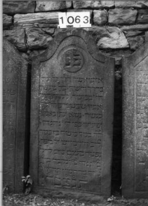 Grabstein 1063 (Index: 99630566) Material: Sandstein Zustand: leicht verwittert Maße HxBxT: 120x58x10 cm Beschreibung: Stele mit Konvexbogenabschluß, Schriftfeld eingetieft: Grabstein 1063