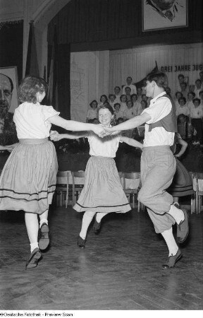 Tänzer in Tracht der Leipziger Eisen- und Stahlwerke, im Hintergrund ein Chor sowie ein Porträt Walter Ulbrichts