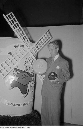 Ein Mann präsentiert zwei Sorten holländischen Käses vor einem Werbeaufsteller in Windmühlenform