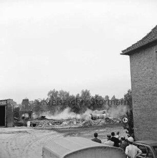 Stadtwerke Bad Oldesloe: Gaswerk: Lübecker Straße: Sprengung des Schornsteins des abgerissenen Kraftwerks: rechts Gebäudeecke: vorn Wagendach und Zuschauer: dahinter rauchender Bauschutt und Gastank: links teilweise abgerissenes Gebäude: hinten Bäume: 10. Juni 1971