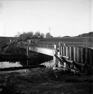 Trave: Brückenbau: Hauptstraße: Landstraße zwischen Klein Wesenberg und Groß Wesenberg: Verbreiterung der einspurigen Brücke: vorn rechts Spundwände: daneben und oben Arbeiter: hinten links Bauwagen, Lieferwagen und Pkws: dahinter Häuser und Bäume