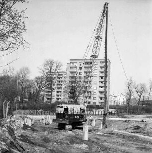 Sülzberg: Bau mehrgeschossiger Wohnblocks: Ramme beim Setzen von Pfählen: rechts daneben Arbeiter: links Zaun: hinten Mitte Hochhäuser am Kurpark: hinten rechts Wohngebäude und Betriebsgelände der Maschinenfabrik Lythall KG