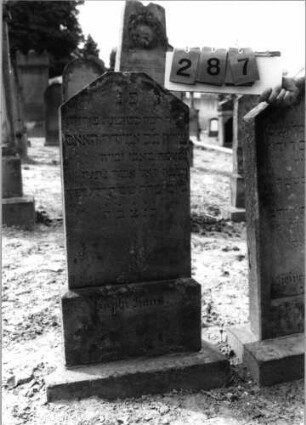 Grabstein 287 (Index: 99797822) Material: Sandstein, weiß Zustand: leichht verwittert Maße HxBxT: 93x41x11 cm Beschreibung: Stele, giebelartig abgeflachter Abschluß, Sockel: Grabstein 287