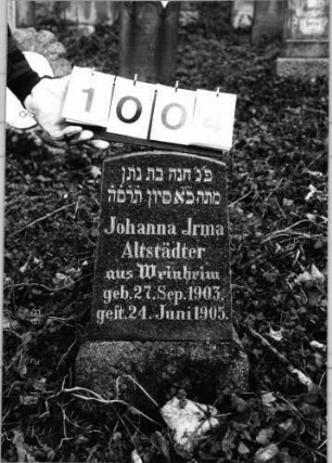 Grabstein 1004 (Index: 99803864) Material: Granit, poliert Zustand: gut Maße HxBxT: 55x26x14 cm Beschreibung: Sockel, Stele mit Flachbogenabschluß: Grabstein 1004