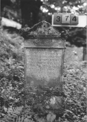 Grabstein 374 (Index: 99799680) Material: Sandstein Zustand: verwittert Maße HxBxT: 97x48x15 cm Beschreibung: Stele, Abdeckplatte mit Giebelaufsatz, Seitenakrotere, unter der Sima Friesband, Schriftfeld eingetieft, getreppter Sockel Symbolik: florale Elemente: Grabstein 374