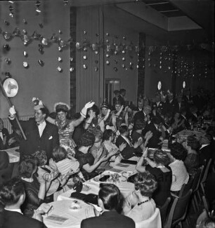 Karneval: Hotel Oldesloer Hof, Saal: Prunksitzung: Veranstalter Oldesloer Männerchor von 1844, Oldesloer Singakademie von 1946: Bühne: Einzug von Tanzmariechen, Mädchengarde, Elferrat, vorweg Zeremonienmeister: Publikum an langen Tischen, gibt Applaus: Bildmitte hinten Saaleingang, 8. Februar 1964