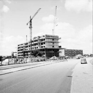 Poppenbütteler Straße: vorne Parplatzflächen, links eine Baustelle, Rohbau eines Wohngebäudes des Heußweges, dahinter Wohngebäude der Segeberger Chaussee: Blick nach Nordwesten
