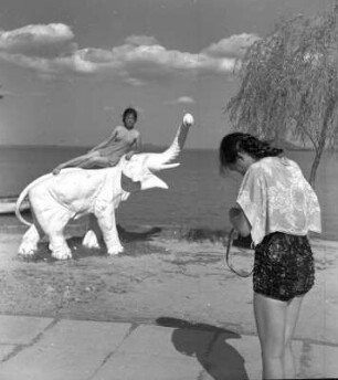 Wuhan (China). Strandszene am Ostsee (East Lake) mit auf Modellelefanten posierender Touristin, die von einer anderen fotografiert wird