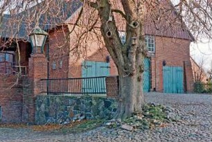 Fritz-Berodt-Straße 7-9: Hofanlage: östliches Wirtschaftsgebäude: Giebelseite mit Scheunentor, Stalltoren, darüber Fassadenplastiken, Fensterband, Giebel mit Verbretterung: an Traufseite Hofüberbauung [angeschnitten] zum westlichen Wirtschaftsgebäude: Hofplatz mit Kopfsteinpflaster: Pfeiler mit Laterne an Hofmauer, Baum