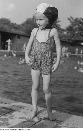 Portrait eines kleinen Mädchens in Badebekleidung am Beckenrand des Freibads stehend